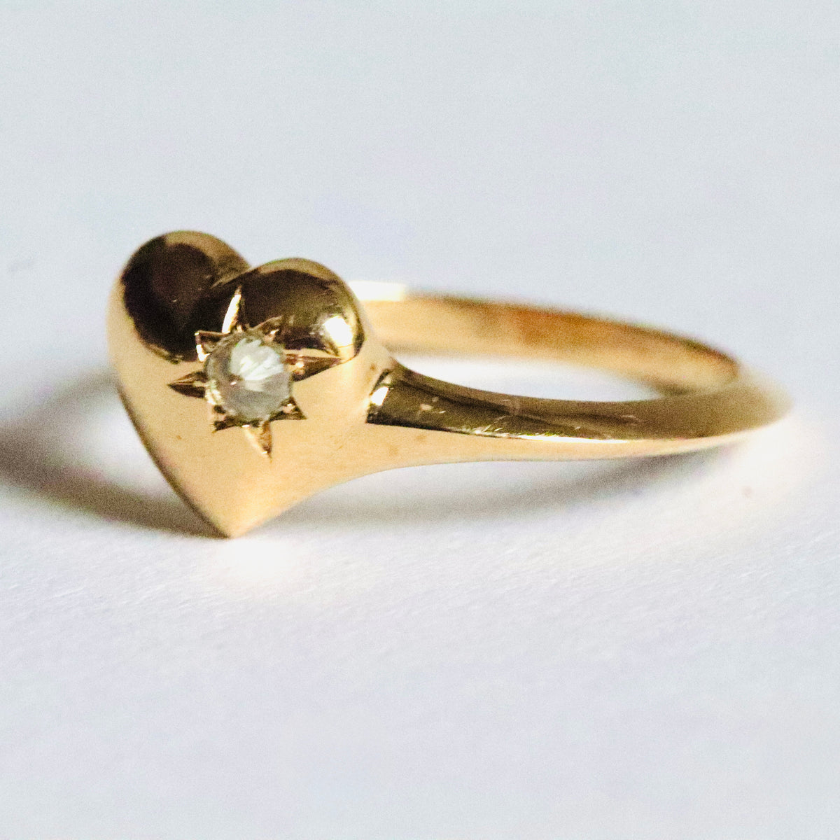 Gold heart-shaped signet ring by Tamsin Rasor, with a star set spiked diamond on the right hand side, shown from the side against a white background