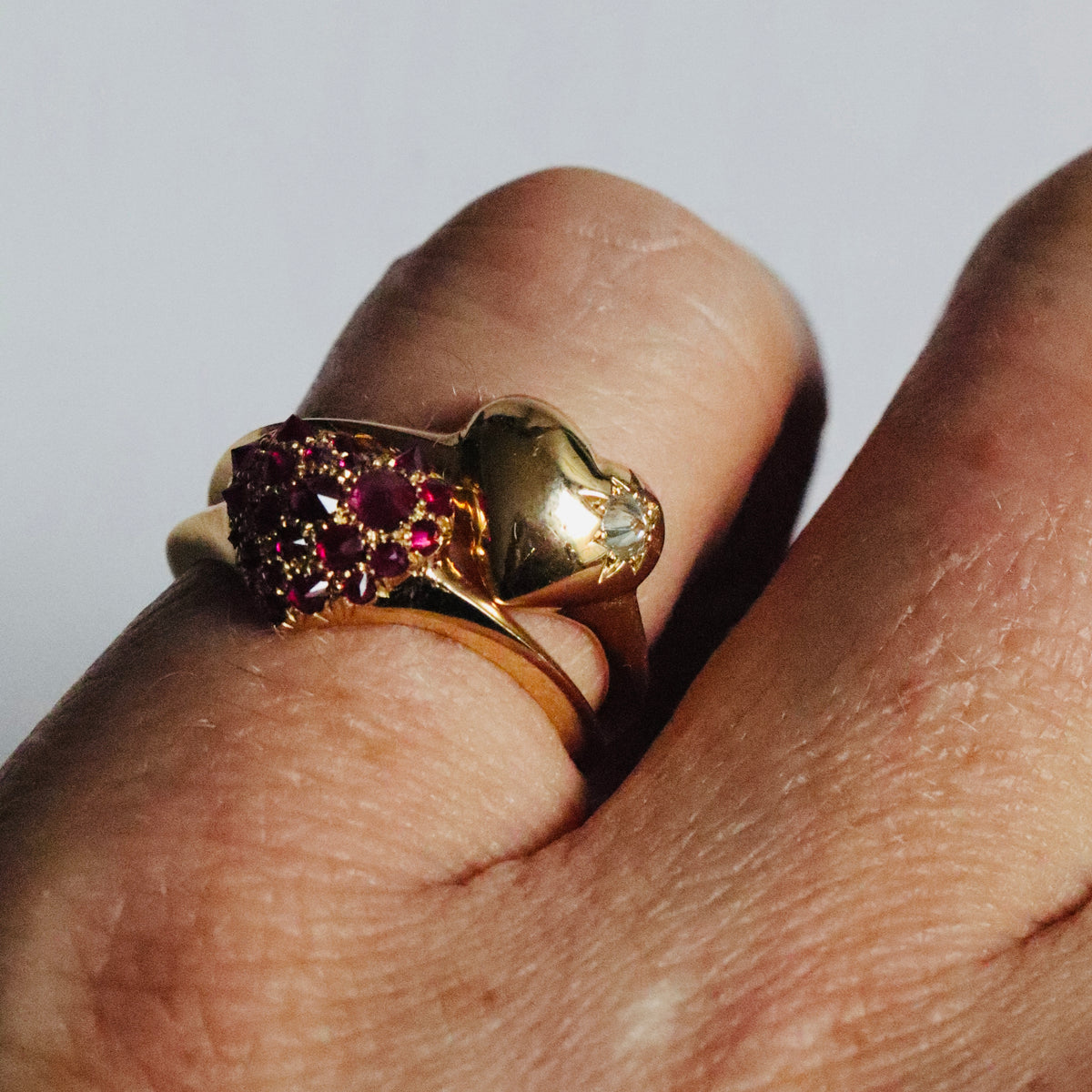 Two gold and gemstone heart shaped signet rings stacked on models pinky finger.