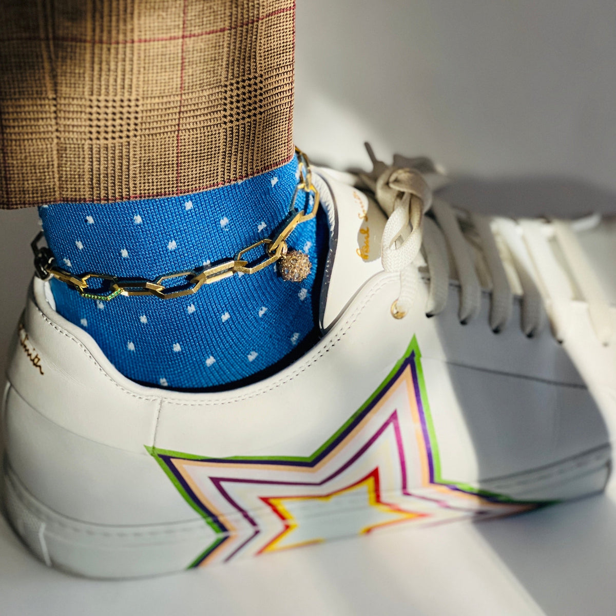 gold and diamond orb charm on gold chain worn as anklet on model wearing blue socks and whire sneakers