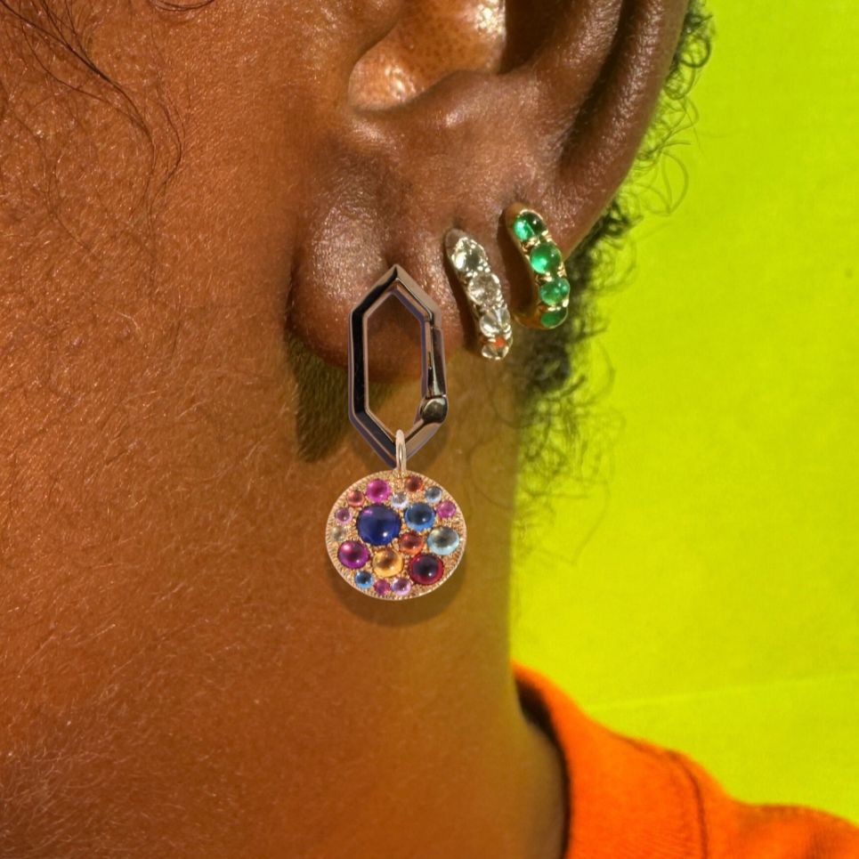 Geometric drop earring with multi color gemstone disc pendant and two gemstone hoop earrings shown on model in orange sweater, against neon yellow background