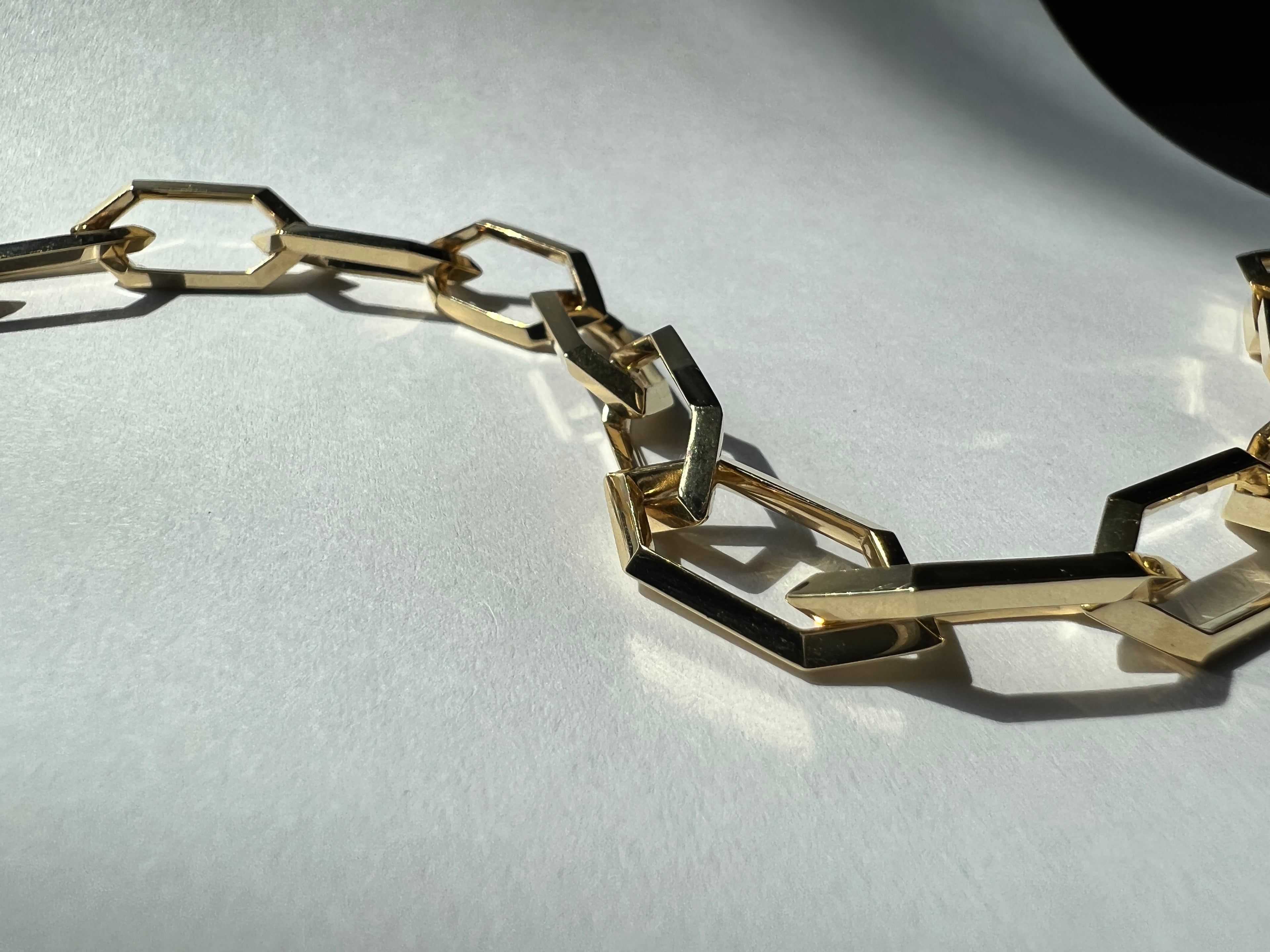 closeup of chunky yellow gold chain necklace with hexagonal links on white papers