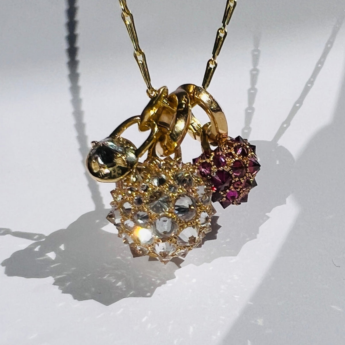 Three gold and diamond charms hanging from gold chain on white background