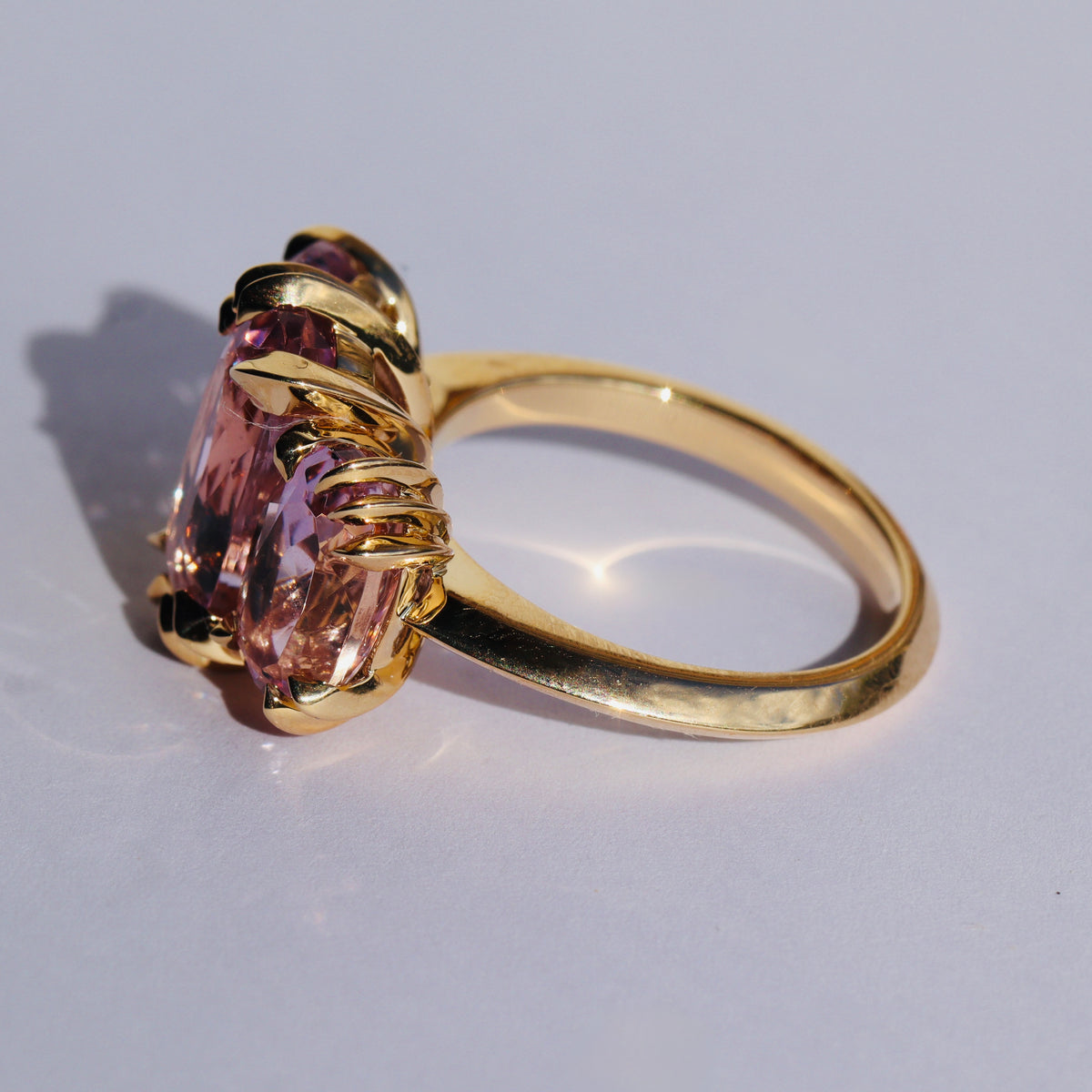 Large cocktail ring with three pink Kunzite gemstones and asymmetric knife edged gold setting, seen from side by Tamsin Rasor, on a white background