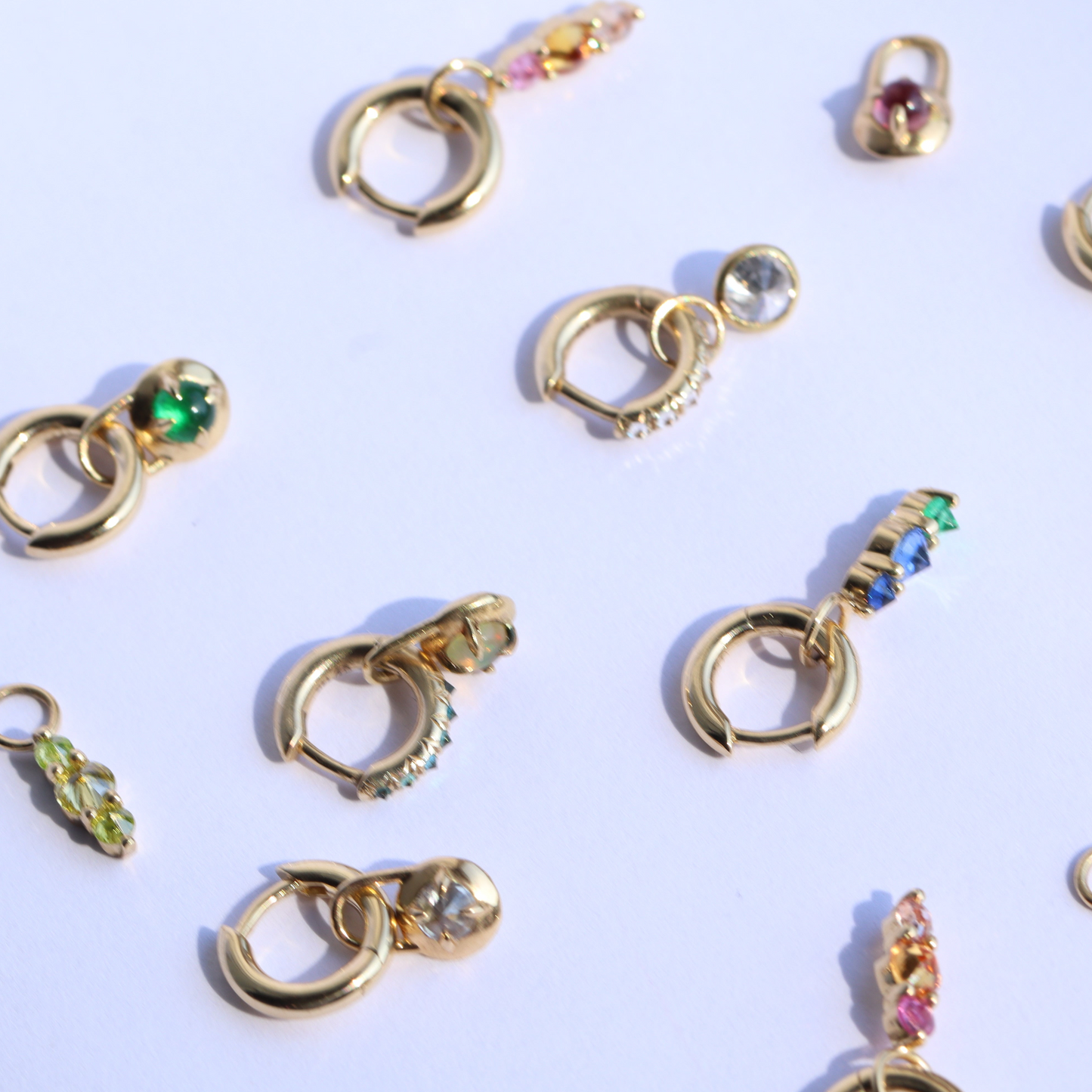 gold hoop earrings with colorful gemstone charms scattered across a white background