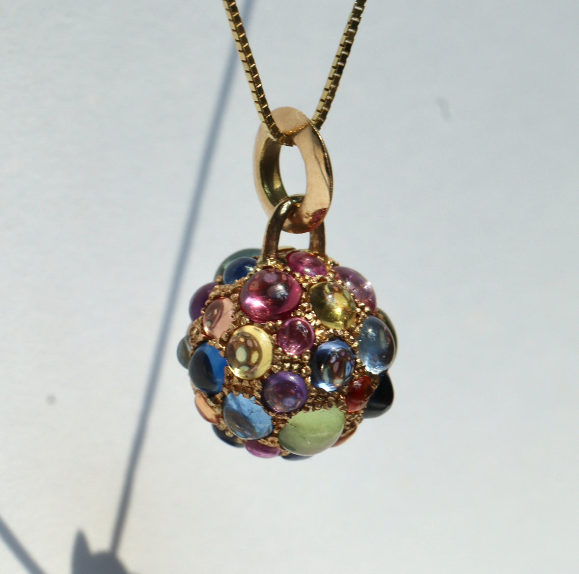 multicolor sapphire cabochon and yellow gold orb charm on gold chain, against white background by Tamsin Rasor