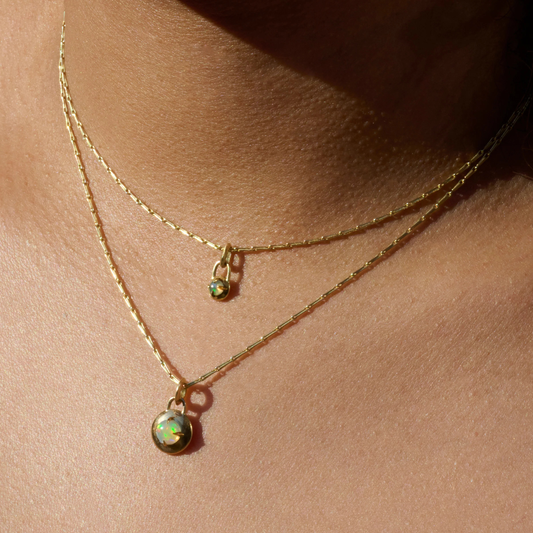 Gold necklaces with a compass pendants featuring a natural opal cabochons stacked around models neck by Tamsin Rasor