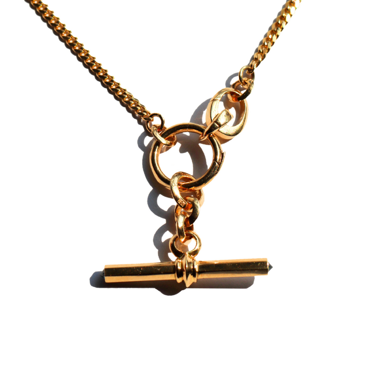 A gold T-Bar pendant with a barbed diamond setting, featuring a blue diamonds, attached to a round clip bail on gold chain , against white background.