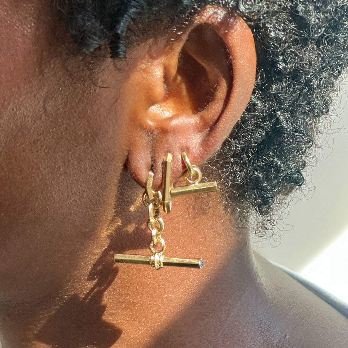 Three Gold T-bar Fob charm and hoop earrings by Tamsin Rasor on model's ear against white background