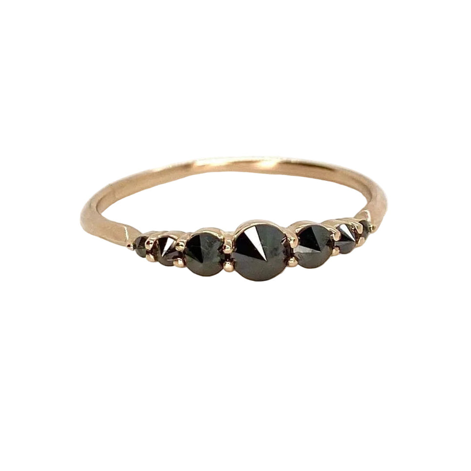 A seven-stone black diamond ring set in a gold band, with a barbed design and a sharp apex on each diamond. Shown on white background