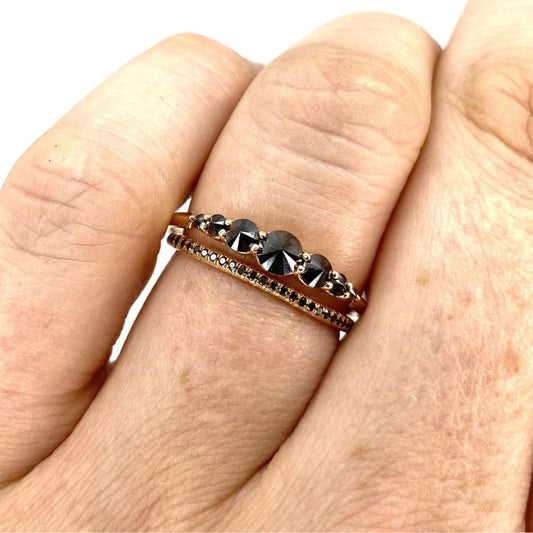 Seven stone black diamond ring stacked with black diamond eternity ring on models finger against a white background