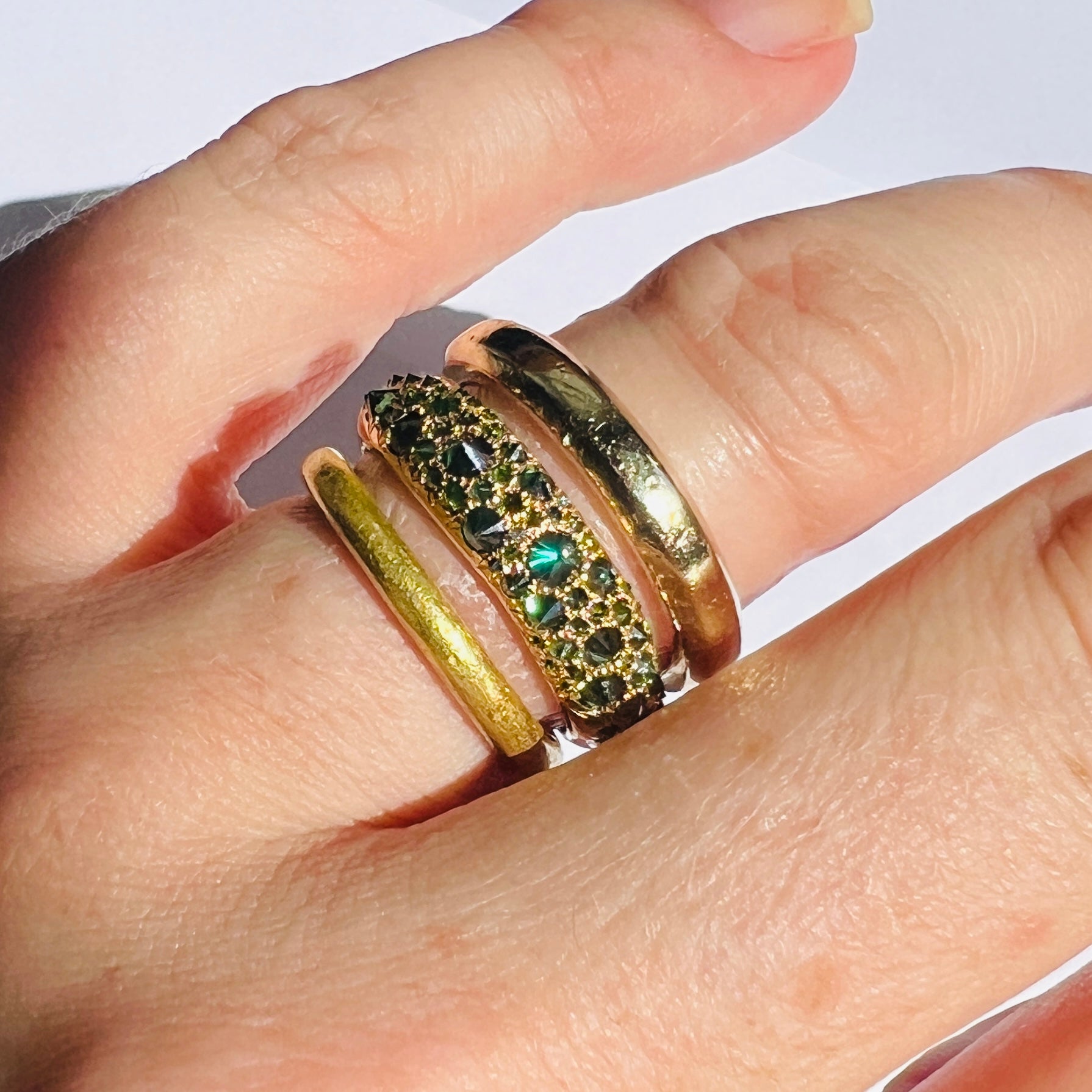 Stack of gold and green diamond rings on models finger on white background