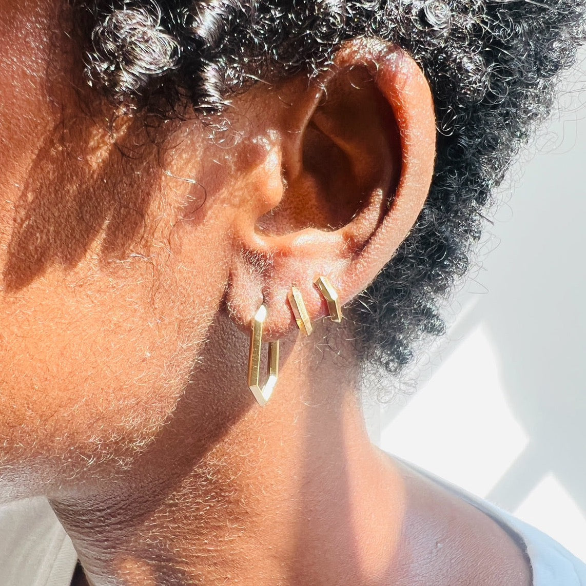 close up of three gold makhaira hoop earrings on models ear