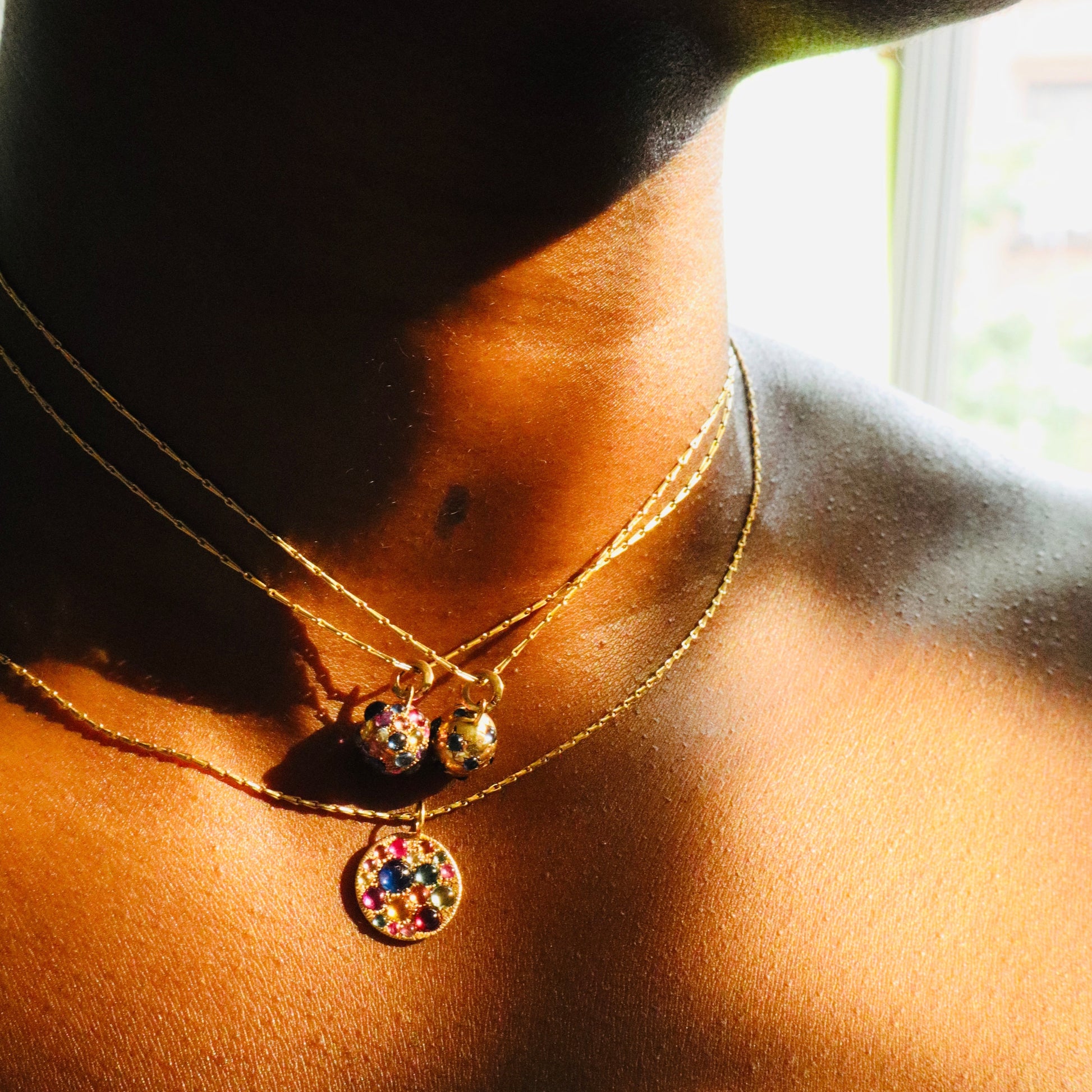 Jelly bean sapphire Orb pendants and jelly bean disc pendant on model against sunlit white background