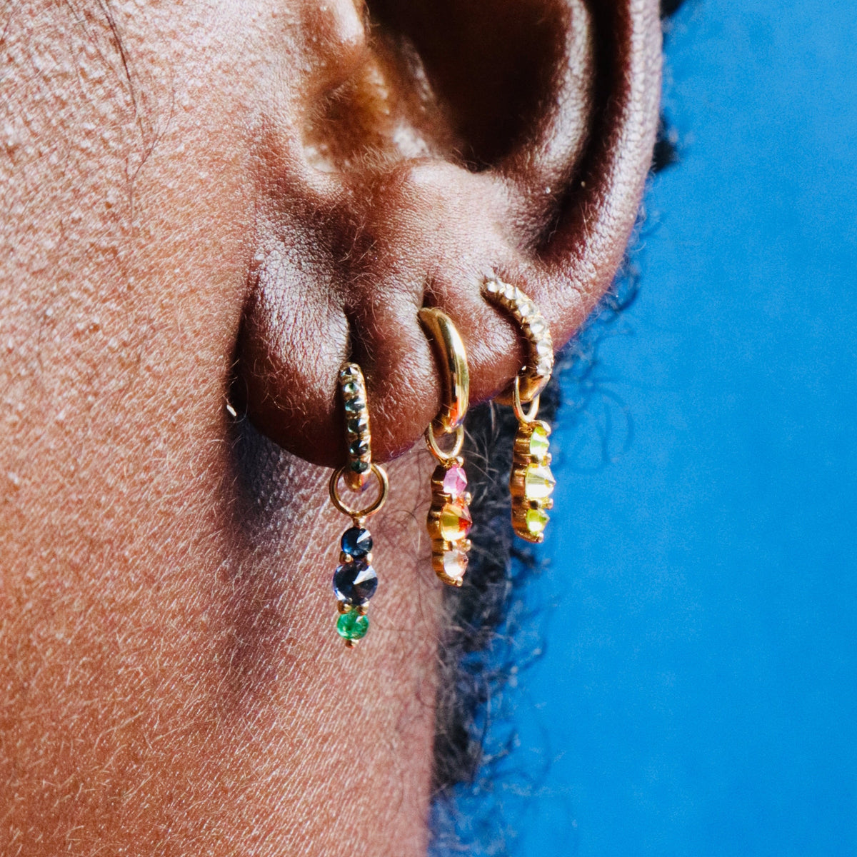 Colorful Barbed Lina charms shown on mini chunky hoop on model's ear against blue background