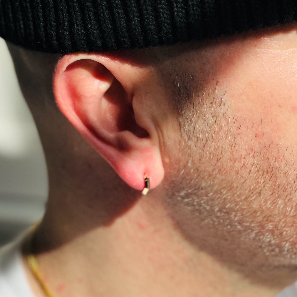 close up of solid gold mini makhaira hoop on male models ear