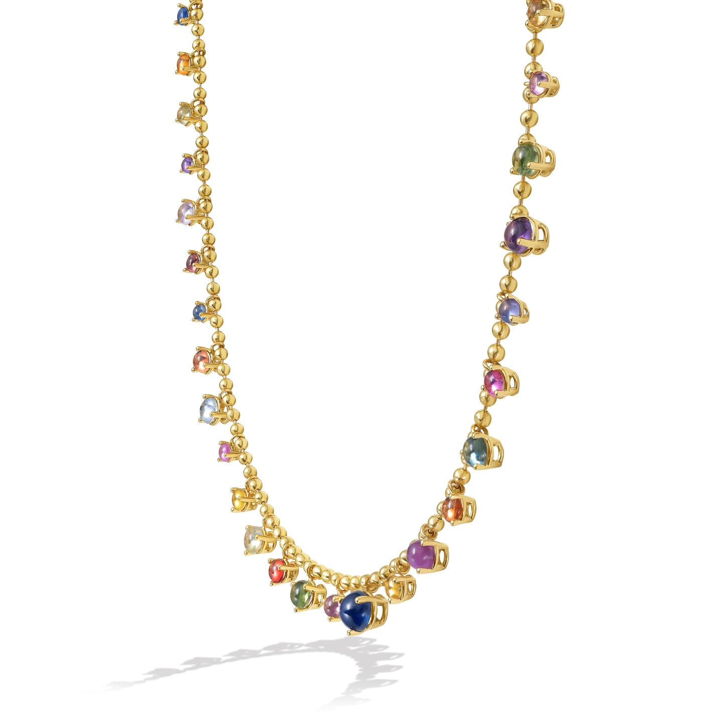 A gold bead chain necklace featuring a fringe of multi color sapphire cabochon gem drops, set in gold prong settings, arranged in a gentle curve against a white background with a soft shadow. By Tamsin Rasor