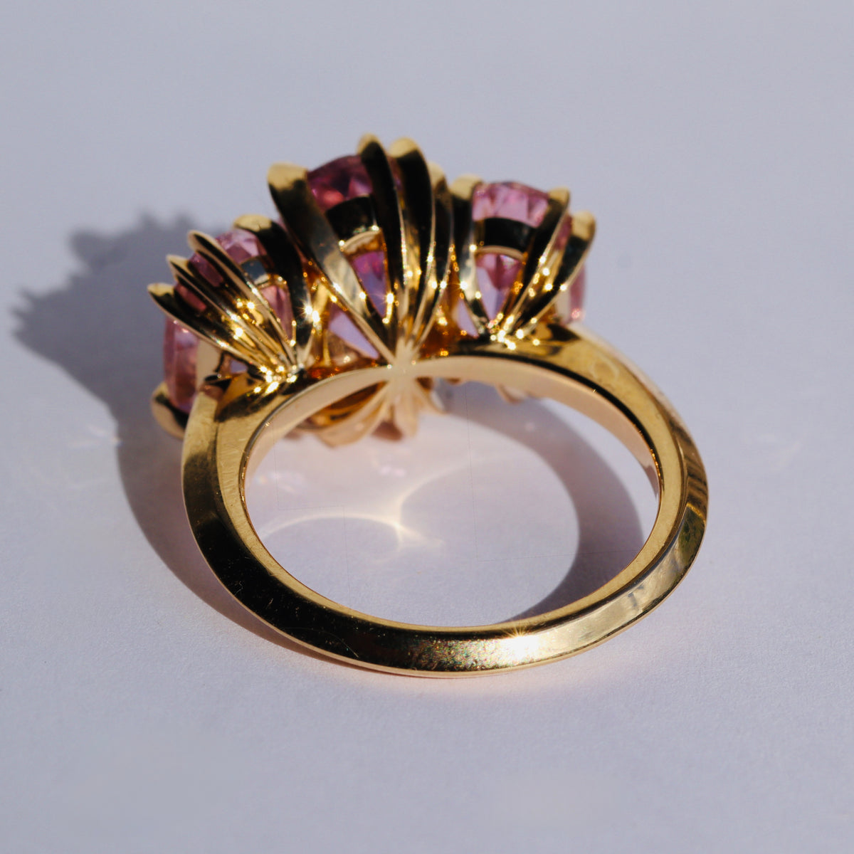 Large cocktail ring with three pink Kunzite gemstones and asymmetric knife edged gold setting, by Tamsin Rasor, seen from rear, on a white background