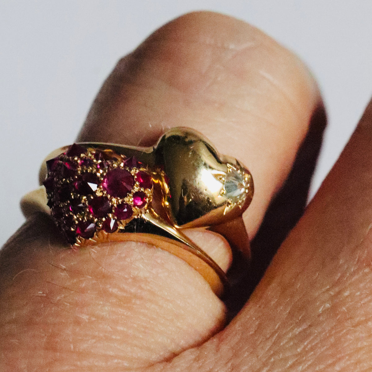 Two gold and gemstone heart shaped signet rings stacked on models pinky finger.