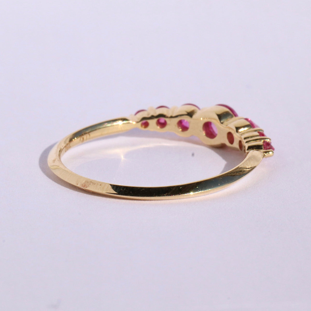 Spiky seven stone ruby and gold ring , from rear, on white background by Tamsin Rasor 
