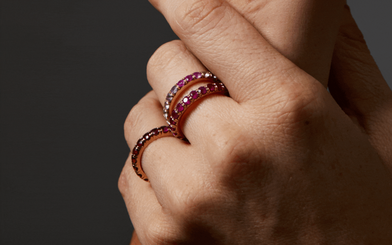 Three ruby eternity rings on hand shown in front of dark grey background