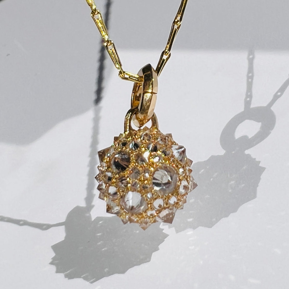 gold and diamond orb charm on gold chain necklace on white background 