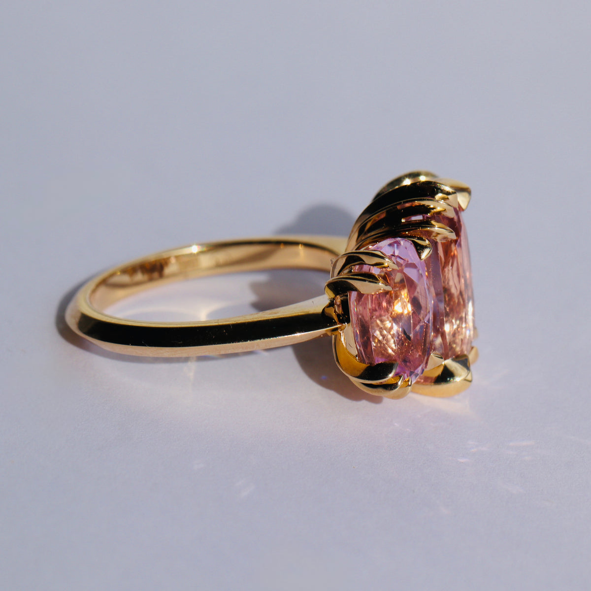 Large cocktail ring with three pink Kunzite gemstones and asymmetric knife edged gold setting, by Tamsin Rasor, see from side on a white background