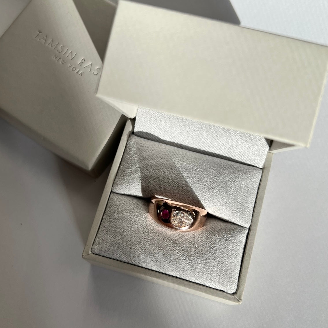 Rose gold , White diamond and pink sapphire ring in open light grey ring box on white and grey background