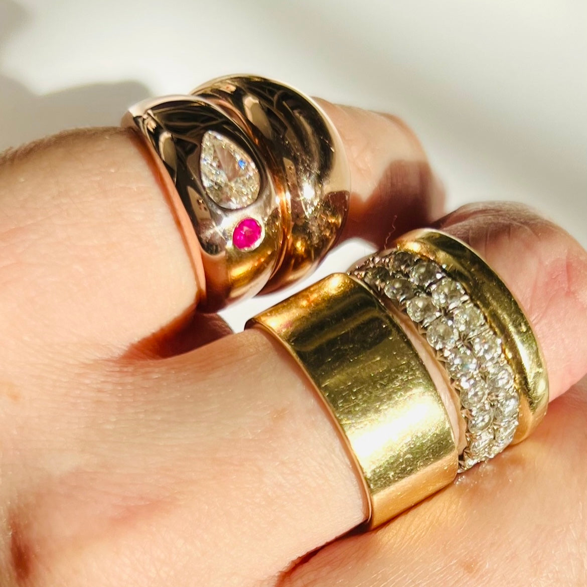 Two domed rose gold pinky rings and two solid yellow gold rings stacked with two white diamond eternity rings shown close up on a hand with a white background