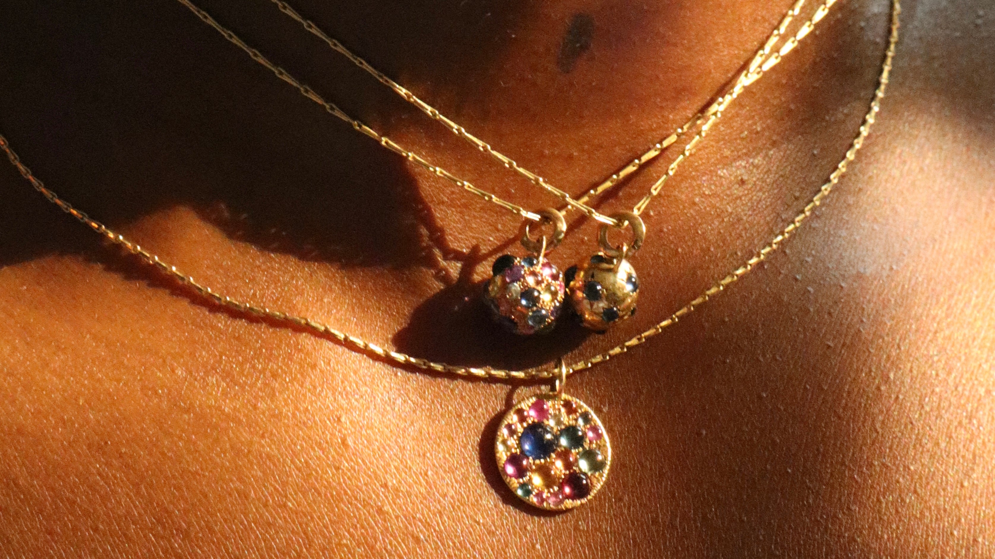 close up of Jelly bean sapphire orbs and disc pendant on layered gold chains around models neck 