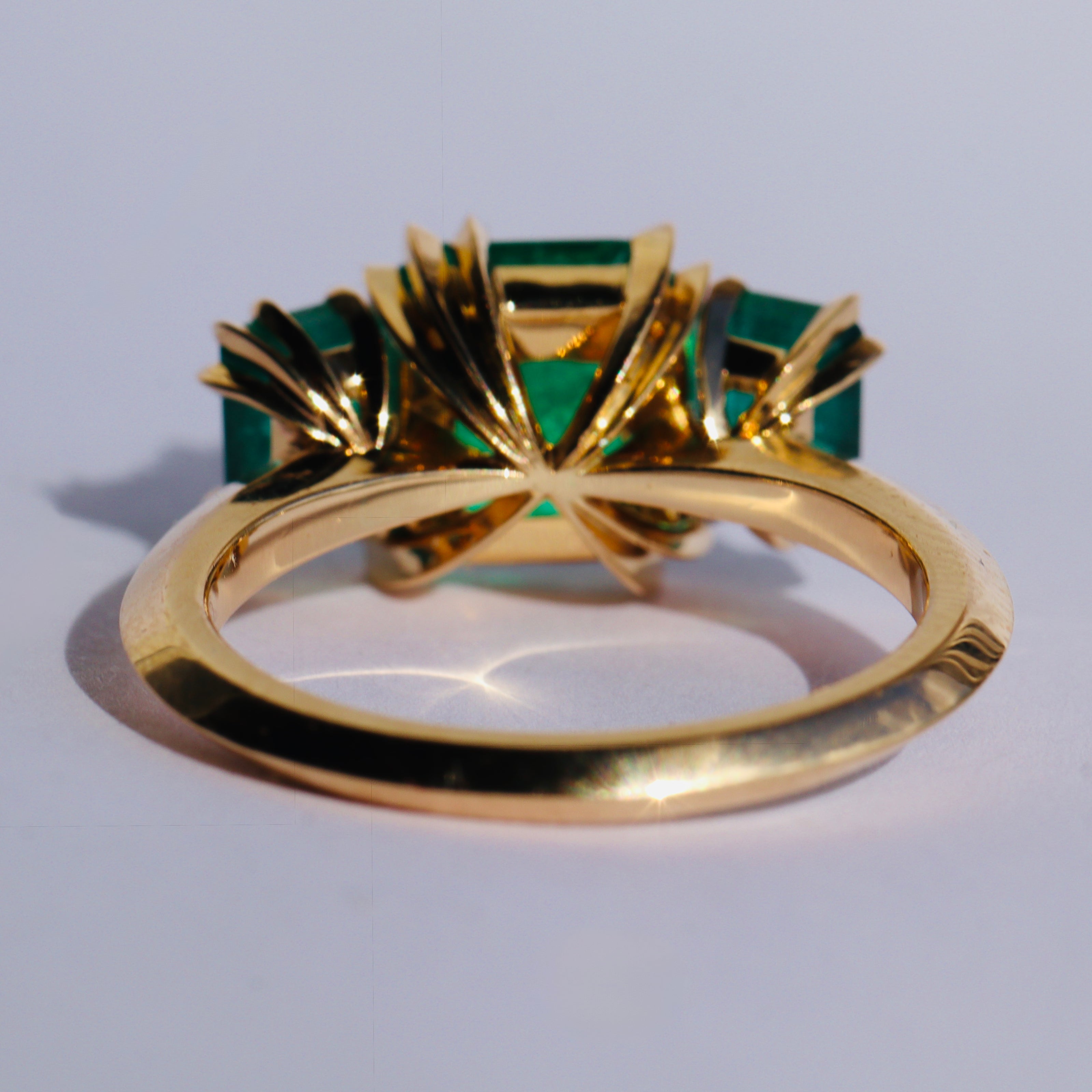 Emerald three stone Makhiara Trilogy ring by Tamsin Rasor in 18K gold seen from behind on a white background 