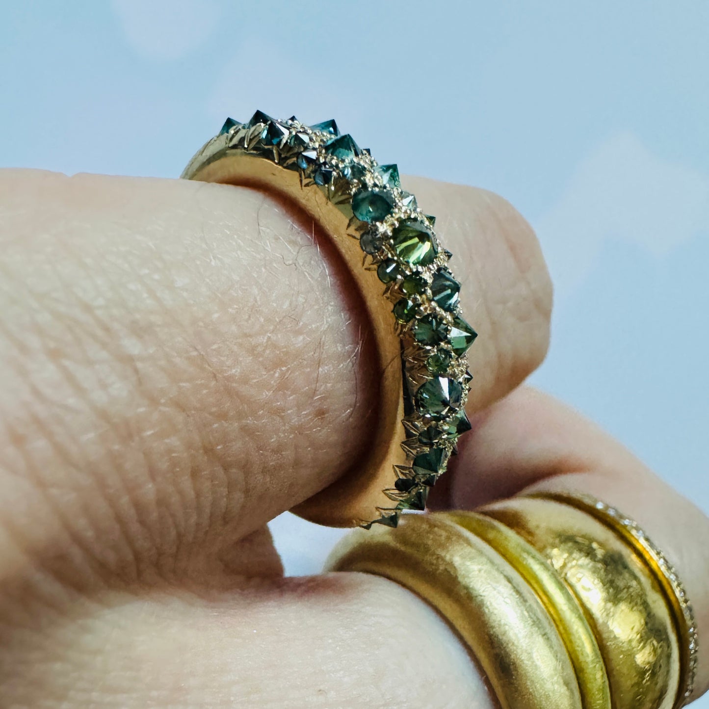 close up of green and blue barbed diamond and 18K gold  medium duomo ring on models pinkie finger 