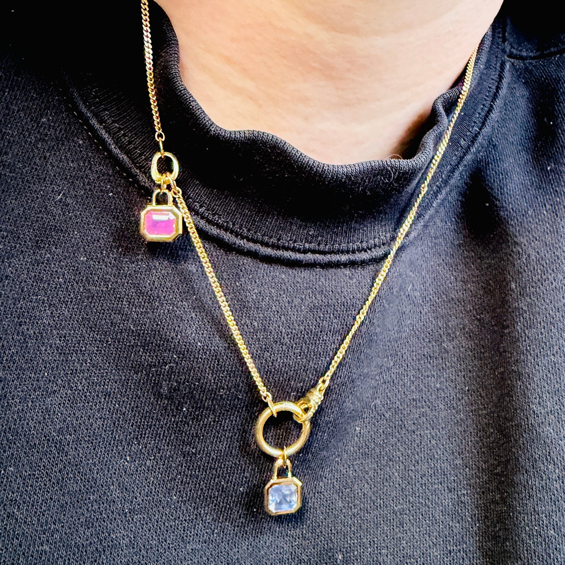 Gold chain with charm clips and two bezel set gemstone pendants. One Pink Spinel and one lavender sapphire worn on model over black sweatshirt