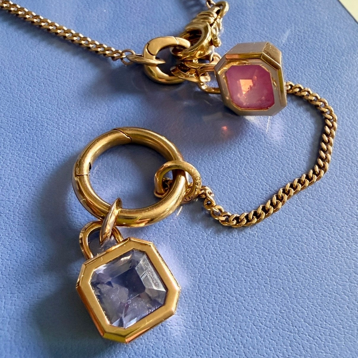 Gold chain necklace with pink spinel and lavender sapphire gemstone charms, displayed on a textured blue surface by Tamsin Rasor.