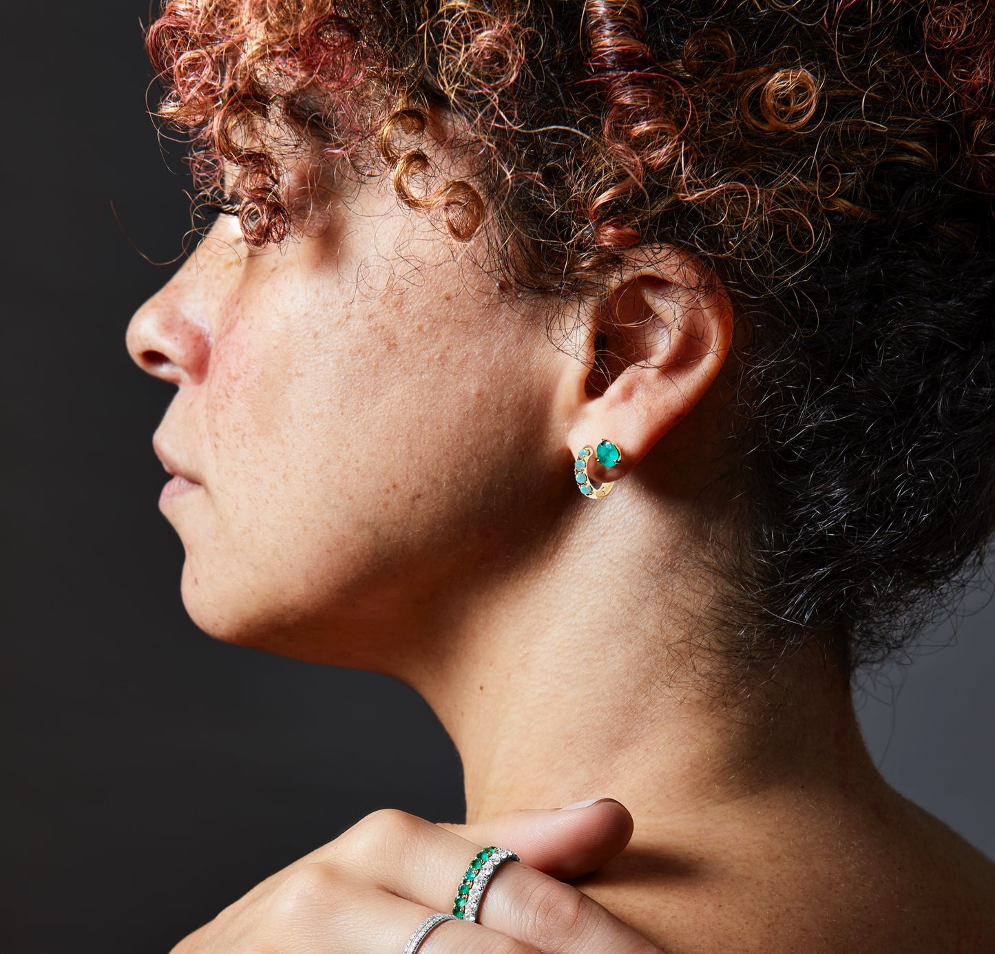 close up of opal hoop earring and emerald stud earring on models ear