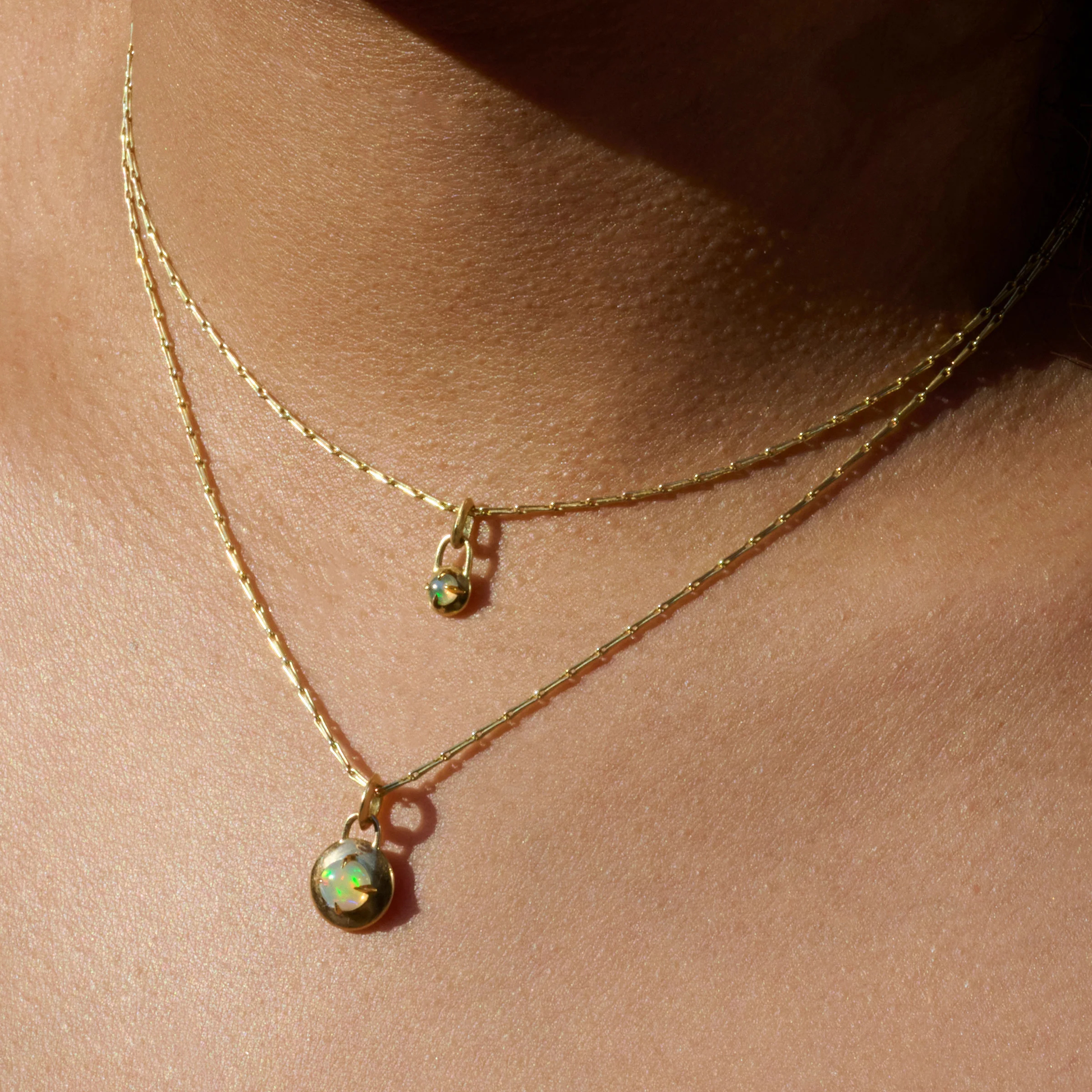 Gold necklaces with a compass pendants featuring a natural opal cabochons stacked around models neck by Tamsin Rasor