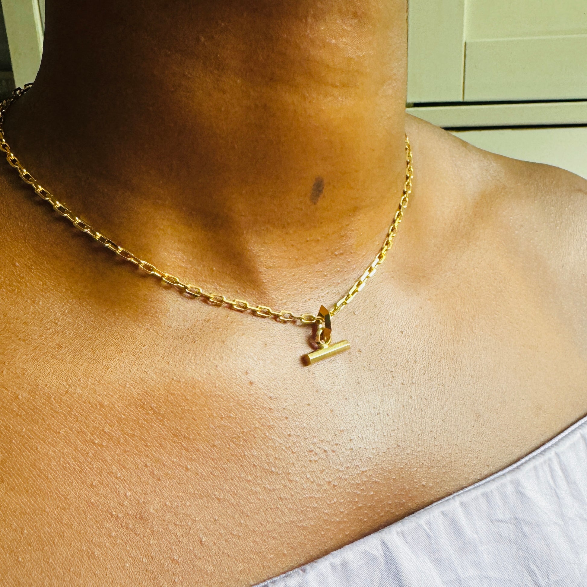 Small Gold T-Bar pendant on chunky gold chain by Tamsin Rasor on model wearing lilac top against white background