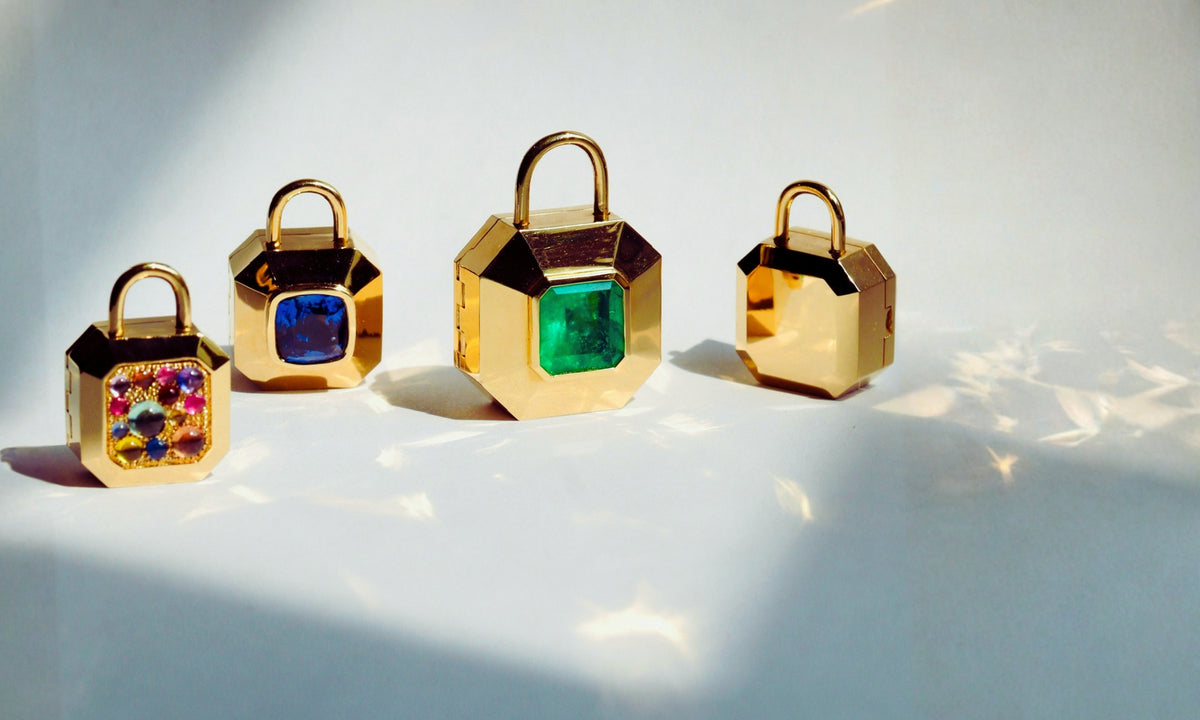 Four gold and emerald and multicolor sapphire gemstone padlock-shaped pendants photographed on a light background