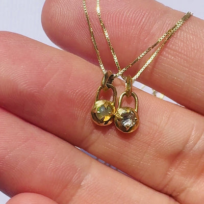 video of two gold necklaces with a compass pendants featuring an opal and a diamond in models hand against a white background by Tamsin Rasor