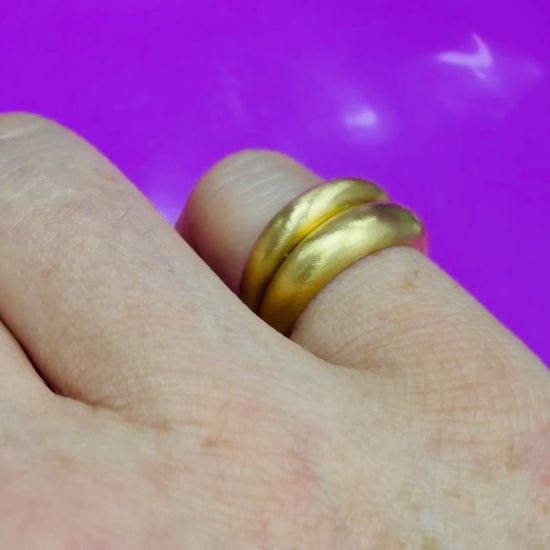 Video of a close up of models hand wearing 2 brushed gold dome rings on their pinky finger against mauve background.