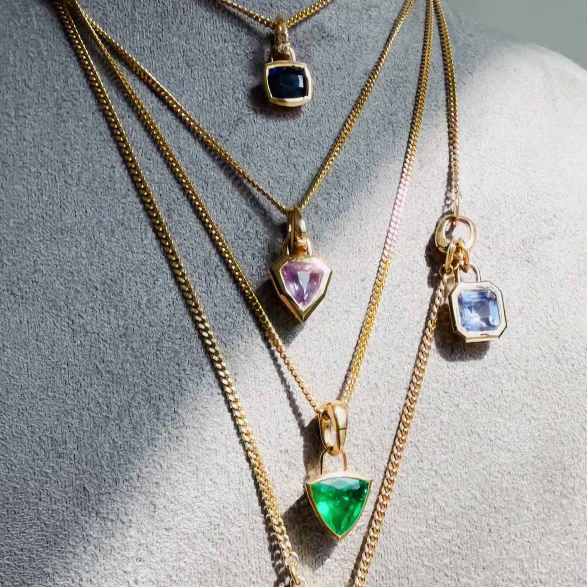 video of colorful gemstone and 18k gold pendants on layered gold curb chains by Tamsin Rasor, on a grey suede neck form