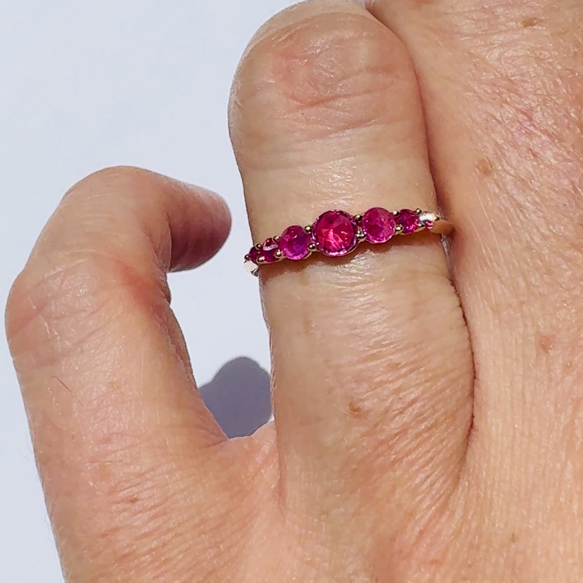 Spiky seven stone ruby and gold ring , on models finger against white background by Tamsin Rasor 