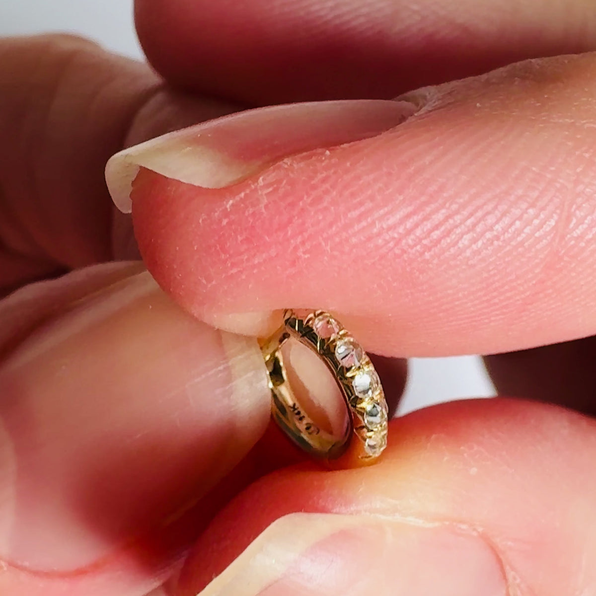 Barbed diamond and gold chunky mini huggie hoop earring held in fingers