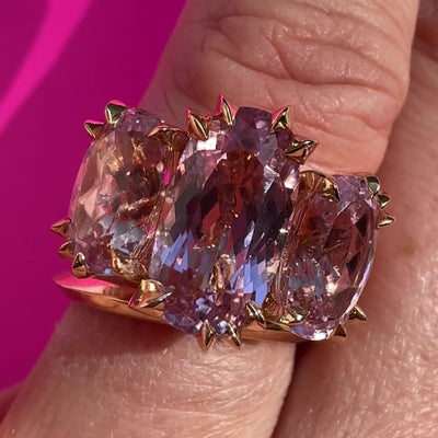 Video of close up of Large cocktail ring with three pink Kunzite gemstones and asymmetric knife edged gold setting on model's hand, by Tamsin. Rasor, against a hot pink background