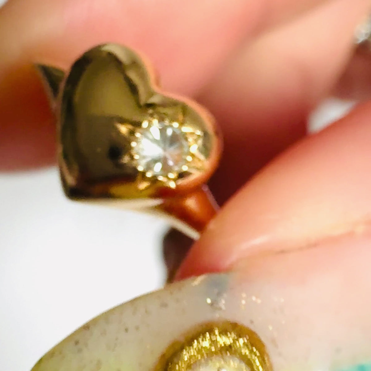 video of gold heart-shaped signet ring  by Tamsin Rasor, with a star set spiked diamond on the right hand side, shown in between models thumb and forefinger