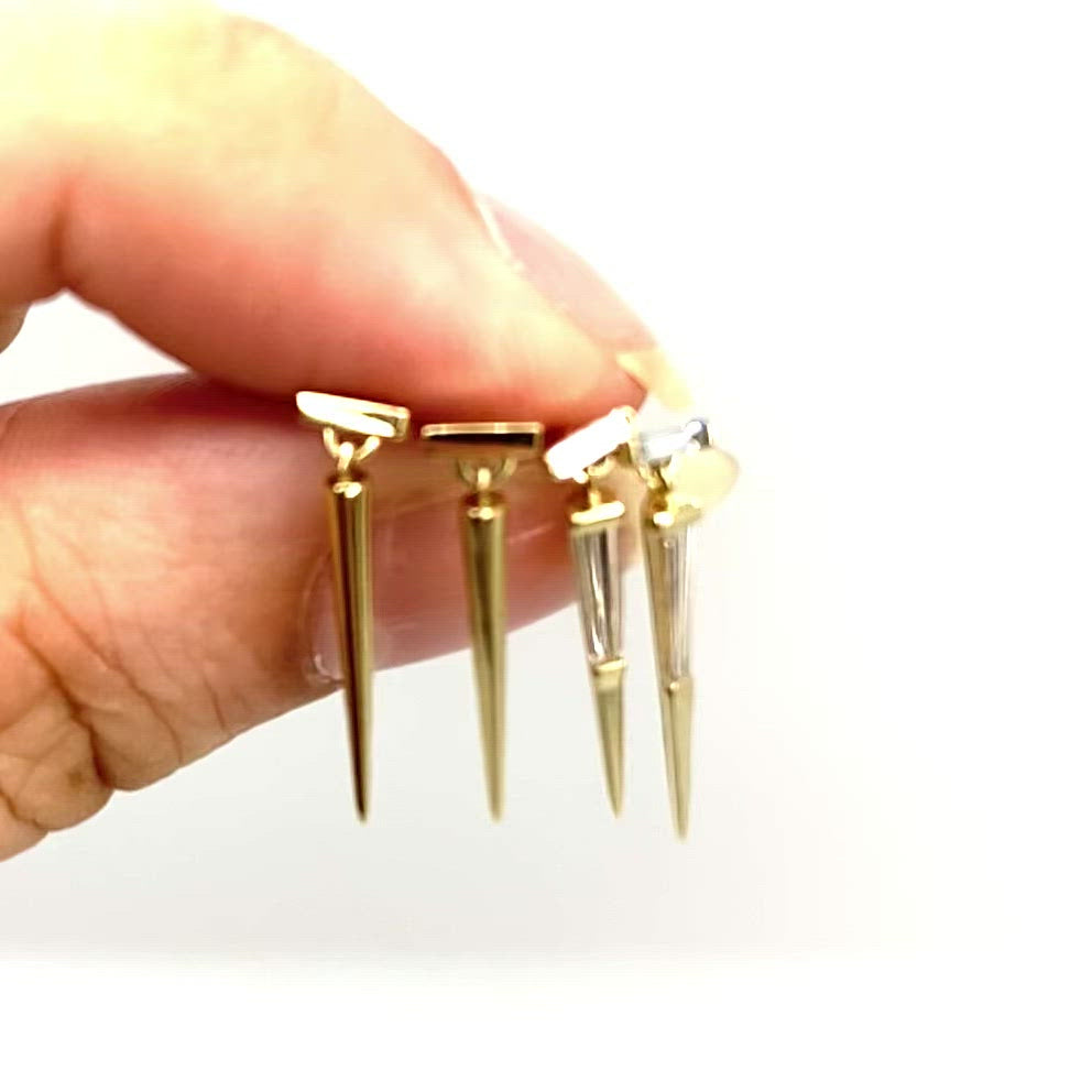 Vidoe of one pair of solid gold and one pair of gold with tapered baguette diamonds,  spike drop earrings in models hand against a white background by Tamsin Rasor