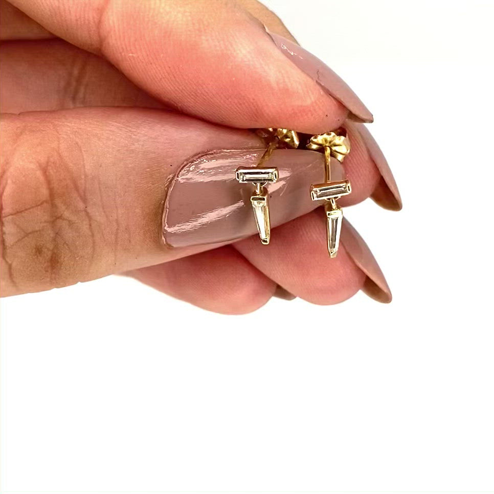 vidoe of a pair of yellow gold drop earrings with baguette cut diamonds, by Tamsin Rasor, in models hand, against a white background