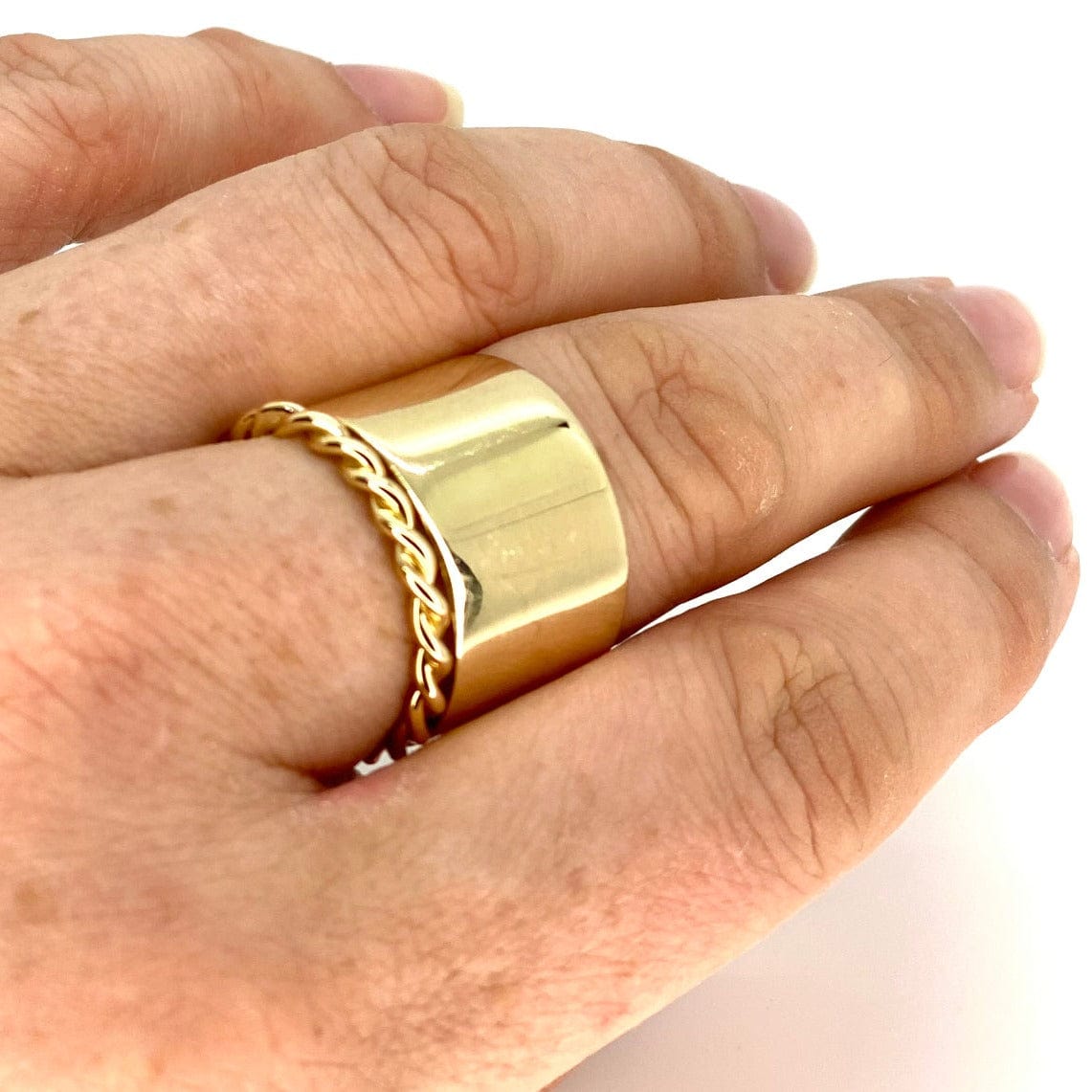 A solid gold twist ring stacked under a solid gold cigar ring on the middle finger of Tamsin Rasor's hand