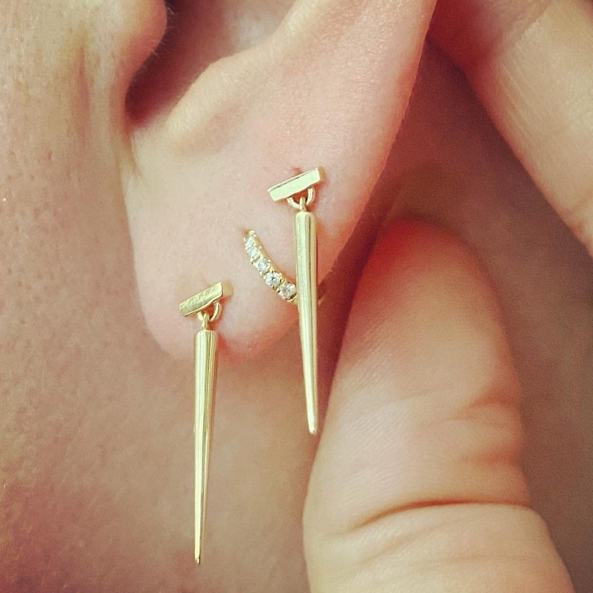 Two Gold spike earrings and one gold and diamond huggie hoop on a models ear by Tamsin Rasor