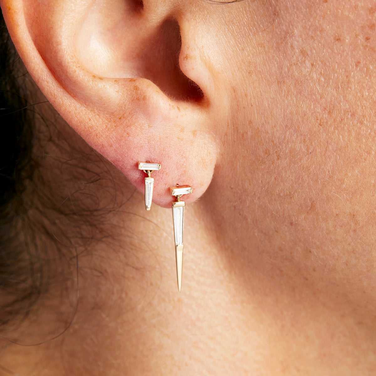 A pair of yellow gold baguette cut diamond drop earrings with a push-back closure on model, by Tamsin Rasor.
